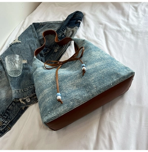 Detail of denim tote bag with brown faux leather trim, drawstring bow and shiny rhinestones