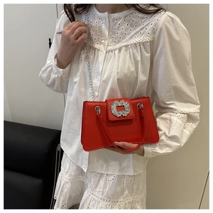 Détail du sac carré rouge avec boucle en strass porté sur une robe blanche élégante
