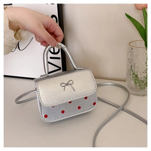 Détail du mini sac argenté à pois rouges avec un nœud métallique sur le rabat