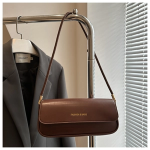 Detail einer braunen Schultertasche mit goldener Aufschrift an einem Kleiderständer