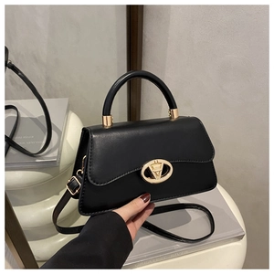 Détail du sac bandoulière noir avec boucle dorée en V tenu par la poignée par un mannequin