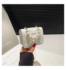 Detail of white heart-quilted crossbody bag with pearl handle and gold chain strap