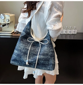 Detail of a large denim tote bag featuring a white bow tie and distressed blue fabric texture