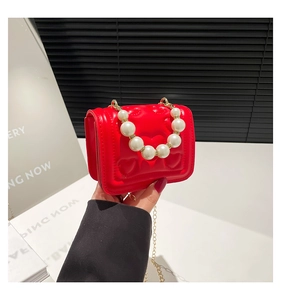 Detail of red mini handbag with heart embossing, pearl handle and gold chain strap