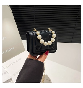 Detail of black heart quilted mini bag with pearl handle and golden chain strap