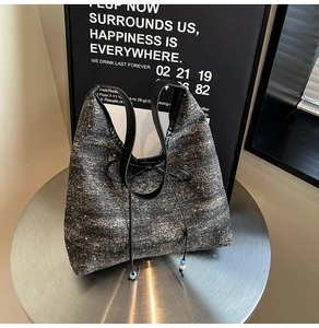 Close-up of black tweed tote bag featuring bow drawstring and bead details on silver table