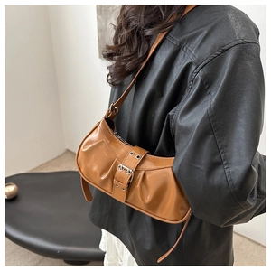 Detail of caramel pleated underarm bag featuring a metallic buckle and glossy finish