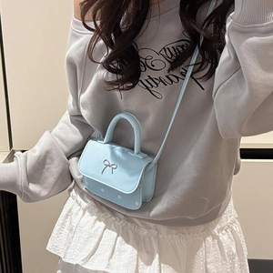 Sac bandoulière bleu clair à pois avec noeud argenté et poignée porté par mannequin