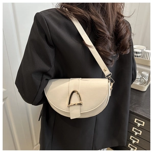 Detail of a cream saddle shoulder bag with gold hardware shown on a model