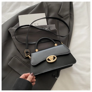 Détail du sac à main en cuir noir avec fermoir doré en V sur fond de blazer gris
