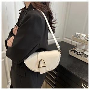 Detail of a creamy white saddle bag with a polished golden horseshoe buckle clasp
