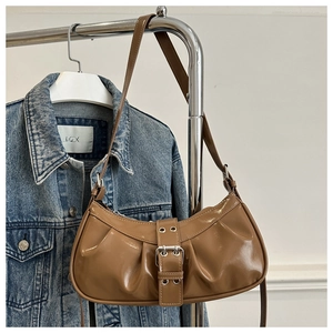 Detail of a brown glossy patent leather shoulder bag with metallic buckle and retro pleats