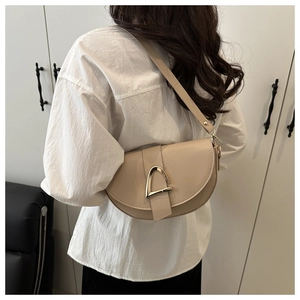 Detail of a beige saddle bag with a golden horseshoe buckle shown on the shoulder
