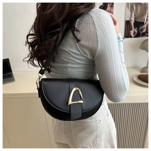 Detail of a black crescent saddle bag with gold D-ring buckle worn on model shoulder