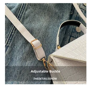 Détail de la texture crocodile blanche et boucle en métal doré sur le sac à bandoulière