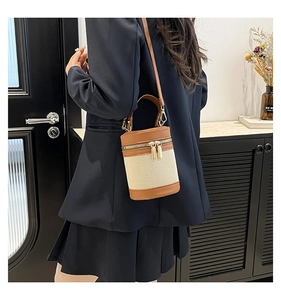 Detail of cylinder bucket bag featuring beige canvas with brown leather trim and gold zippers