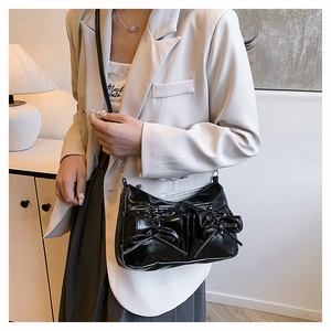 Détail d'un sac à bandoulière en cuir verni noir avec poches à nœuds et fine chaîne argentée