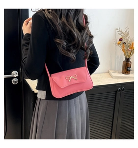 Rear view of a model wearing a pink shoulder bag with a gold bow accent and leather texture