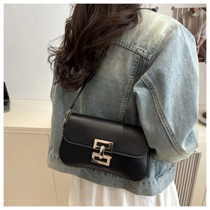 Detail of minimalist black leather crossbody bag featuring a golden geometric clasp