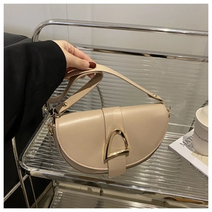 Close-up of beige saddle bag featuring a bold gold D-buckle and premium smooth leather finish