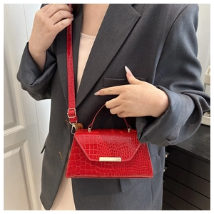 Détail du sac rouge à motif crocodile avec boucle dorée sur un blazer gris chic