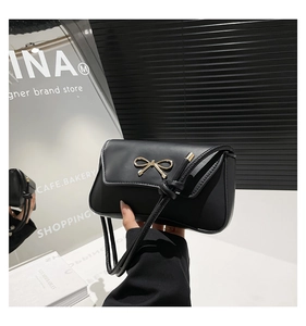 Close-up of black matte leather bag with elegant golden bow hardware and knotted strap