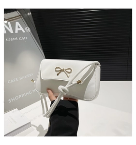 Close-up of white crossbody bag with golden bow hardware and matte leather texture