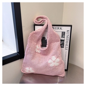 Close-up of pink knit tote bag with large white floral crochet and artistic hollow design