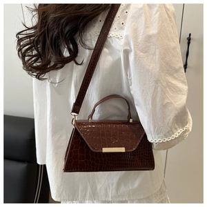 Détail du sac à main marron foncé motif crocodile avec fermoir doré sur chemise dentelle