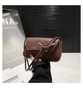 Detailed view of brown flap shoulder bag with gold bow buckle and adjustable knotted strap