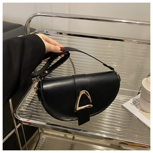 Detail of minimalist black leather saddle bag featuring a textured golden metal clasp