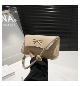 Detail of light beige baguette bag featuring a gold metal bow clasp and knotted strap