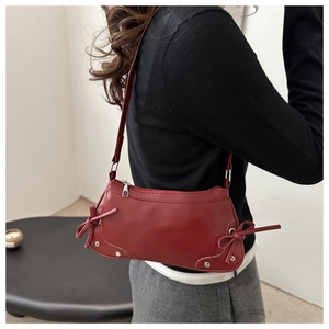Side view of red faux leather baguette bag with silver studs and side bow details