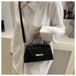 Détail d'un sac bandoulière noir motif crocodile avec fermoir doré porté par un modèle