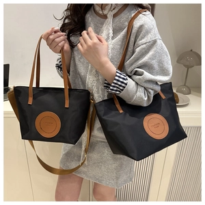Black nylon tote bag with brown leather handles and adjustable wide strap detail