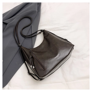 Deep brown Hobo bag with zip detail and metal pendant on elegant fabric background