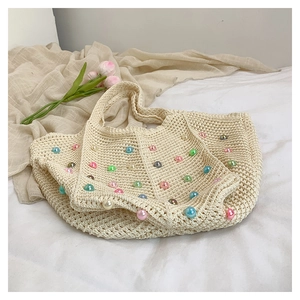 Close-up of beige crochet tote bag with colorful pearl accents on soft fabric