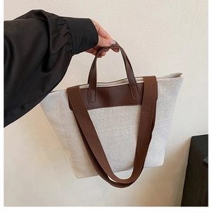 Detail of off-white canvas tote bag with brown leather handles and woven shoulder strap