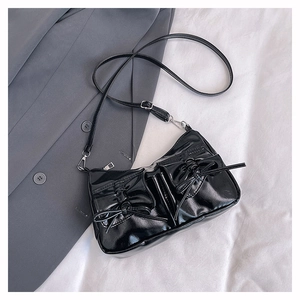 Detail of glossy black patent leather shoulder bag featuring decorative double ribbon bows
