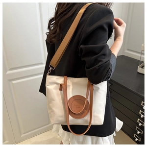 Detail view of beige nylon tote bag with brown straps and fashion patch worn by model