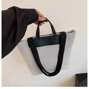 Detail of canvas tote bag showing contrast leather handles and wide shoulder strap