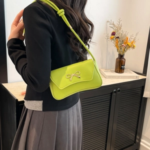 Neon green baguette shoulder bag with gold bow clasp worn by a model in a modern room