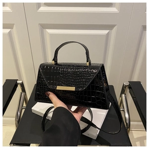 Détail d'un sac à main noir motif crocodile avec boucle dorée devant un fond moderne chic