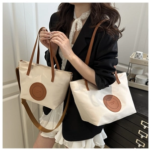 Detail of off-white canvas tote bag with brown leather handles and brand emblem