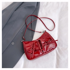 Detail of a dark red shoulder bag with dual front pockets and a decorative bow