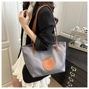 Detail of gray nylon tote bag with leather shoulder strap and fashion circular logo patch
