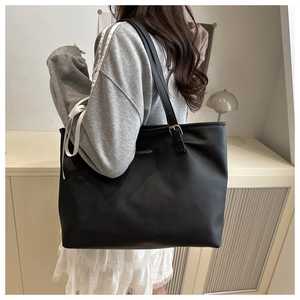 Detail of a large black tote bag with golden FASHION print worn on a model's shoulder
