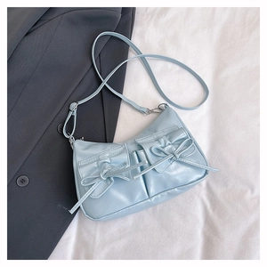 Detail of light blue crossbody bag with bow pockets on a grey blazer over white fabric