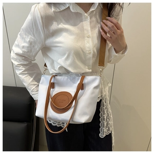 Detail of white nylon tote bag with brown leather handles and a wide shoulder strap