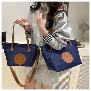 Detail of dark blue nylon tote set with brown leather straps and fashion bags logo label